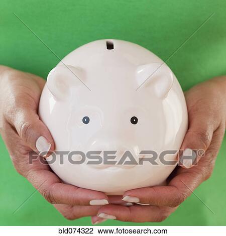 Stock Image - Close up of African woman holding piggy bank. Fotosearch