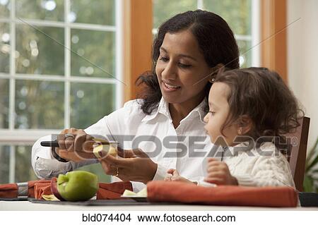 Picture - Indian woman slicing apple for daughter. Fotosearch