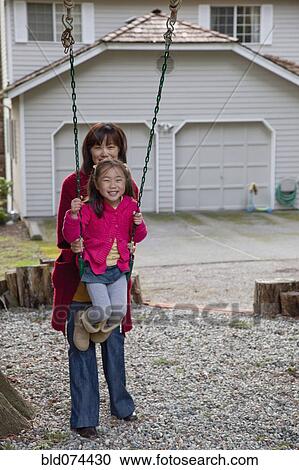 Stock Image - Korean mother pushing daughter on swing. Fotosearch