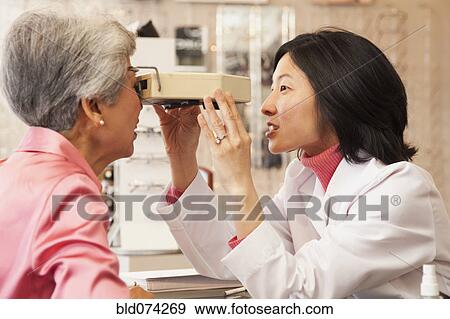 Stock Photo - Korean optician giving woman eye exam. Fotosearch