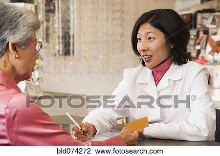 Stock Image - Korean optician talking to customer. Fotosearch