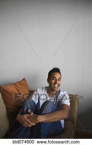 Stock Image - Mixed man sitting on sofa laughing. Fotosearch
