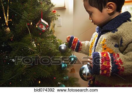 Stock Image - Mixed race boy decorating Christmas tree. Fotosearch