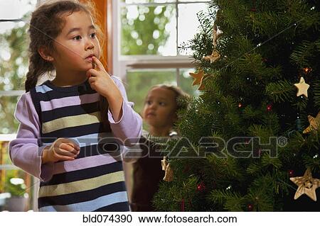 Stock Image - Mixed race girl decorating Christmas tree. Fotosearch
