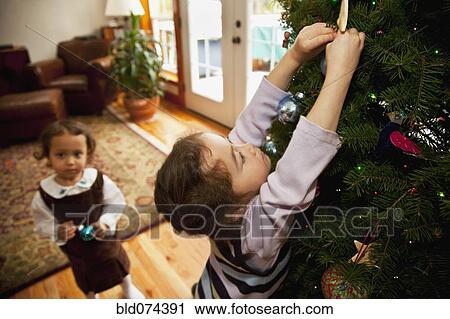 Stock Image - Mixed race girl decorating Christmas tree. Fotosearch