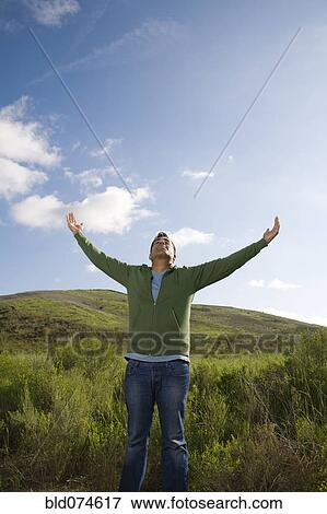 Stock Photo - Mixed race man in field with arms outstretched. Fotosearch