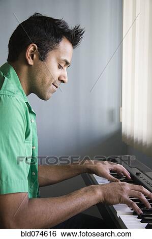 Stock Photograph - Mixed race man playing electric keyboard. Fotosearch