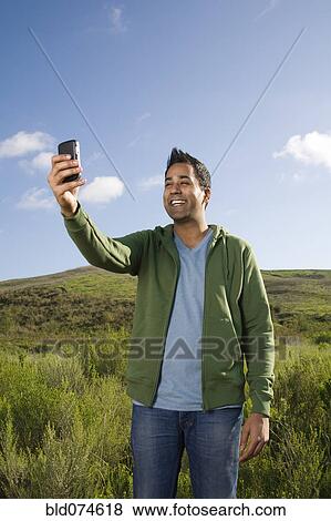 Stock Photo - Mixed race man taking photo with cell phone. Fotosearch