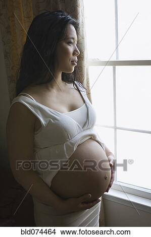 Pregnant Asian woman standing near window View Large Photo Image Picture - Pregnant Asian woman standing near window. Fotosearch