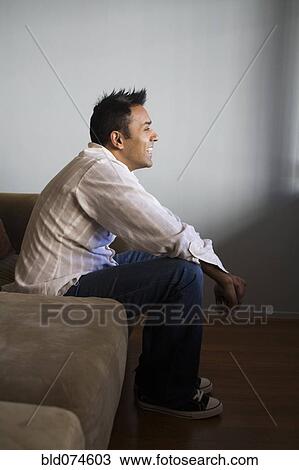 Stock Image - Smiling mixed race man sitting on sofa. Fotosearch