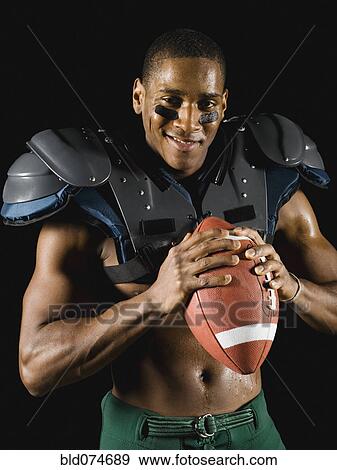 Stock Photo - African football player holding football and wearing protective pads. Fotosearch