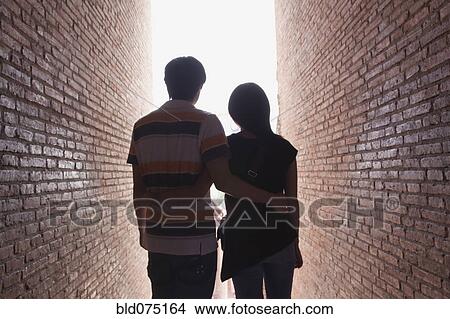 Picture - Asian couple walking between brick walls. Fotosearch