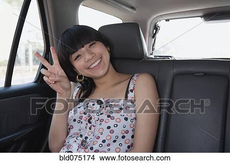 Picture - Asian woman gesturing peace sign in back seat of car. Fotosearch