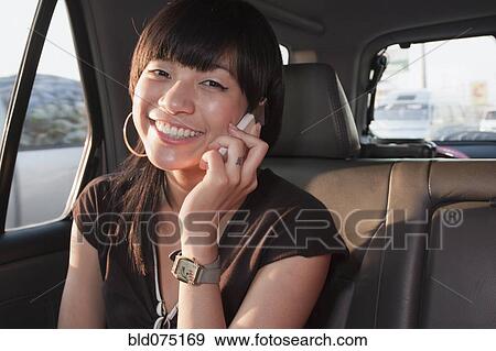 Asian woman talking on cell phone in back seat of car View Large Photo Image Stock Photo - Asian woman talking on cell phone in back seat of car. Fotosearch