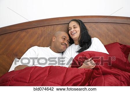 Stock Image - Dominican man lounging in bed with wife. Fotosearch