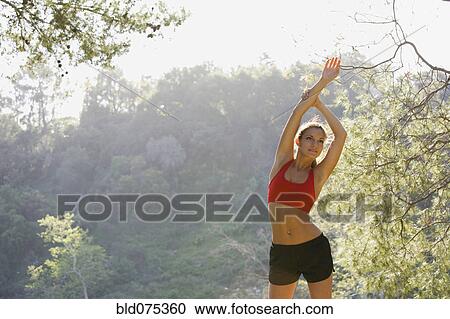 Stock Image - Hispanic woman stretching arms overhead. Fotosearch