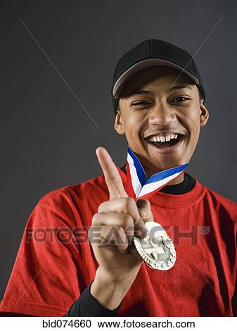 Stock Image - Mixed race baseball player gesturing with award medal. Fotosearch