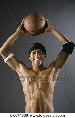 Stock Photograph - Mixed race basketball player holding ball overhead. Fotosearch