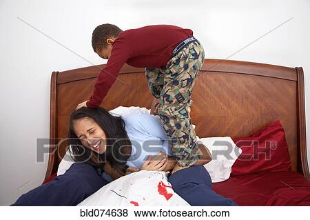 Stock Photo - Mixed race boy tackling parents in bed. Fotosearch