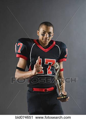 Stock Image - Mixed race football player holding trophy and gesturing. Fotosearch