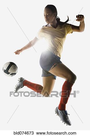 Stock Image - Mixed race soccer player kicking soccer ball in mid-air. Fotosearch