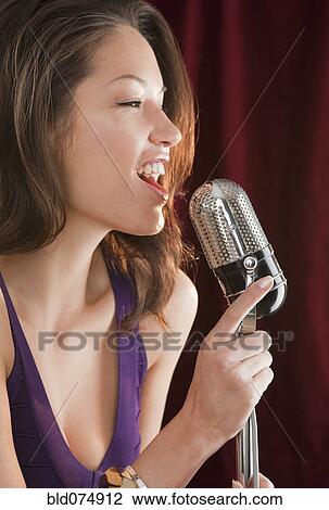 Stock Image - Mixed race woman singing into microphone. Fotosearch