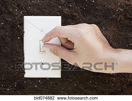 Stock Image - Woman flipping light switch in soil. Fotosearch
