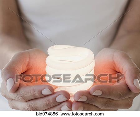 Stock Photograph - Woman holding glowing compact fluorescent bulb. Fotosearch