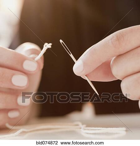 Stock Image - Woman stringing frayed thread through needle. Fotosearch