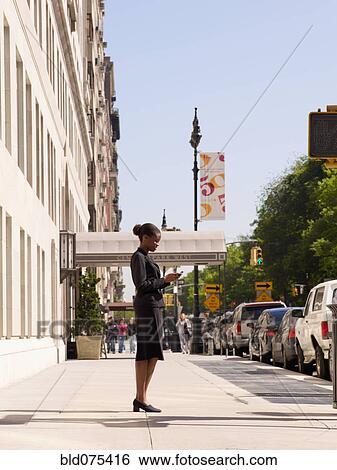 African businesswoman looking at cell phone on sidewalk View Large Photo Image Stock Photograph - African businesswoman looking at cell phone on sidewalk. Fotosearch