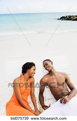 African couple sitting in lounge chairs on beach View Large Photo Image Stock Photo - African couple sitting in lounge chairs on beach. Fotosearch