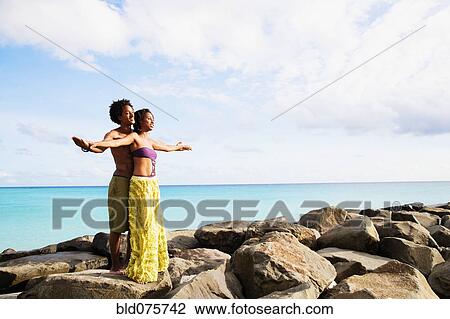 Stock Image - African couple standing on rocks by ocean. Fotosearch