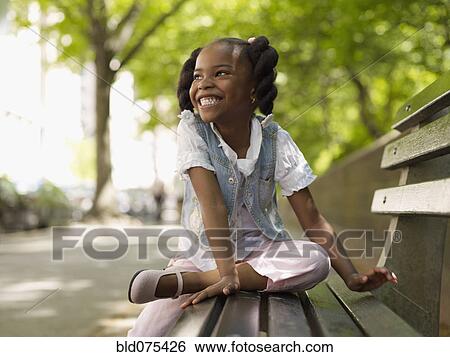 Stock Photograph - African girl smiling on bench. Fotosearch
