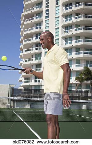 Stock Image - African man balancing tennis ball on racket. Fotosearch