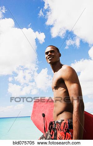Stock Photography - African man holding body board on beach. Fotosearch