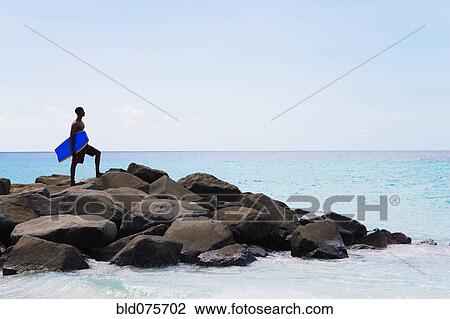 African man holding body board on rocks in ocean View Large Photo Image Stock Image - African man holding body board on rocks in ocean. Fotosearch