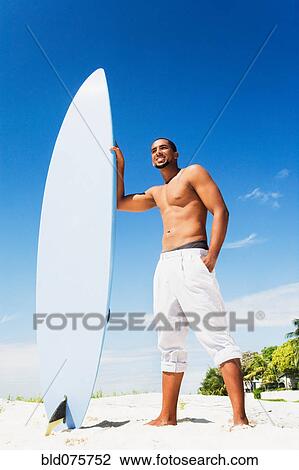 African man holding surfboard on beach View Large Photo Image Stock Image - African man holding surfboard on beach. Fotosearch
