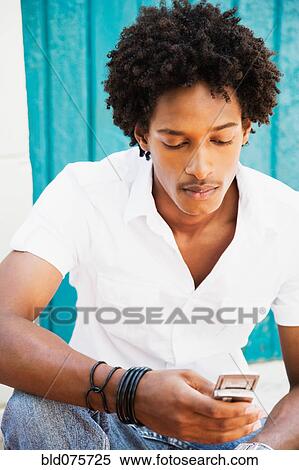 Stock Photography - African man looking down at cell phone. Fotosearch