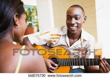 Stock Image - African man playing guitar for woman. Fotosearch