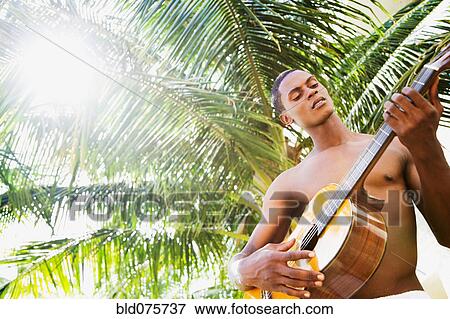 Stock Photo - African man playing guitar in front of palm tree. Fotosearch