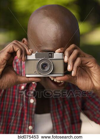 Stock Image - African man taking photograph with retro camera. Fotosearch