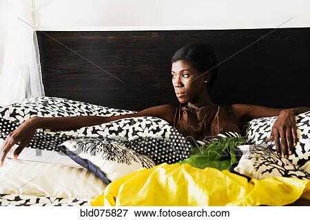 Stock Photo - African woman laying on bed and looking pensive. Fotosearch
