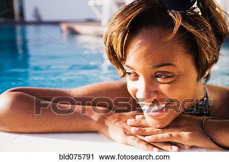 Stock Image - African woman leaning on edge of swimming pool. Fotosearch