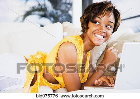 Stock Photograph - African woman using laptop on sofa. Fotosearch