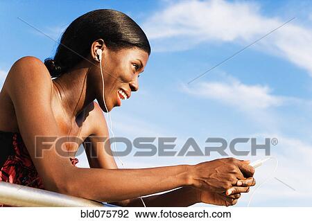Stock Image - African woman wearing headphones and holding MP3 player. Fotosearch