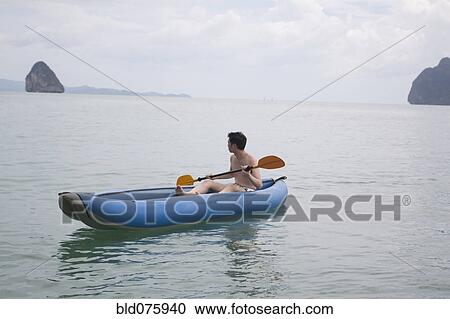 Stock Image - Chinese man paddling boat in ocean. Fotosearch