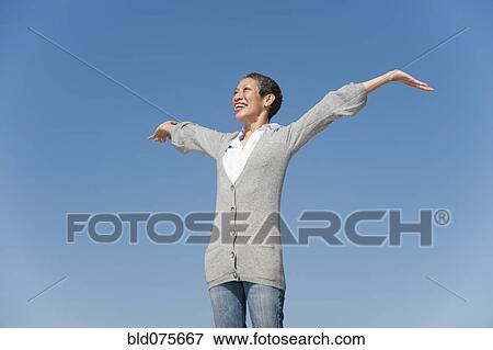 Chinese woman smiling with arms outstretched against blue sky View Large Photo Image Stock Photo - Chinese woman smiling with arms outstretched against blue sky. Fotosearch