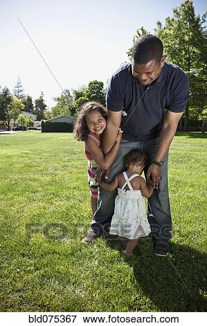 Stock Photo - Father and daughters playing in park. Fotosearch