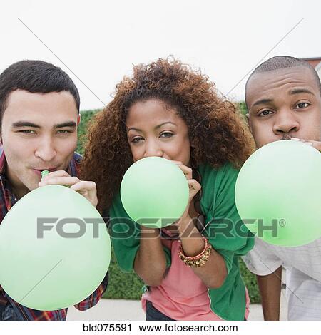 Stock Image - Friends blowing up green balloons. Fotosearch