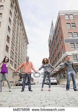 Stock Photograph - Friends holding hands and standing in a row on urban street. Fotosearch